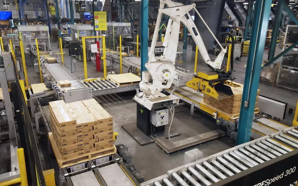 TRFSpeed 300 robot placing cases on a pallet beside a roller conveyor, in a cast iron plant