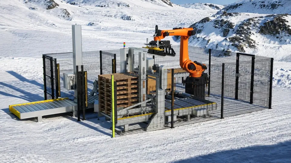 TRFSubzero palletizing cell with fencing and an orange robot stacking cases on a pallet in a snowy cold environment
